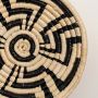 A closeup view of the natural and black rattan wall decor plate showing its detailed woven texture and geometric handcrafted pattern for warm earthy home styling.