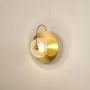 Brass wall light with textured clear glass shade glowing softly against plain white backdrop.