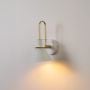 Elegant white wall sconce with golden arm glowing softly on white background enhancing warmth in home interiors.