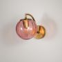 Modern brass wall light with pink glass globe shade displayed against clean white wall backdrop.