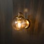 Modern grey glass wall light with brass fixture glowing warmly against black background interior.