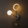 Decorative black and gold wall light with glowing frosted glass globe illuminated on dark backdrop.