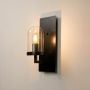Contemporary black metal wall sconce with glass dome shade glowing warm light on black background for home interior lighting.