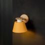 Wooden wall sconce with yellow conical lampshade glowing warm light on black background for bedroom study and kids room modern wall lighting.