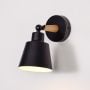 Modern wooden wall sconce with black conical lampshade glowing warm light white background for bedroom hallway and study stylish wall lighting decor.