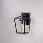 Black metal lantern wall light with clear glass shade and exposed bulb shown off on white background for modern home decor.