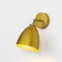 Modern gold wall sconce with metallic dome shade mounted beside curtains on soft green wall.

