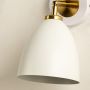 A closeup of a white metal wall light set against a soft beige surface revealing its smooth curved shape and offering minimal elegant modern décor.