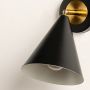 Closeup view of black and gold metal wall sconce highlighting its conical shade smooth finish and warm bulb design for modern decorative lighting decor.