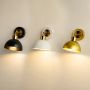 Three dome shaped wall sconces in black white and gold mounted on a light wall each with a warm glowing bulb.