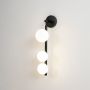 Contemporary black wall sconce with three frosted glass globes glowing softly displayed on plain white background for product showcase.