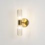 Modern gold wall sconce with double textured glass tube shades glowing softly photographed on plain white background product view.