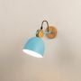 A blue Scandinavian wall light with a matte dome shade and wooden mount shown with the light on against a clean white background giving a warm soft glow.