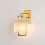 Modern gold wall sconce with rectangular textured glass shade glowing warmly photographed on plain white background product view.