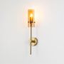Elegant gold wall light glowing with cylindrical glass shade photographed against white background for modern interior styling.