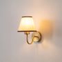 Gold metal wall sconce with beige fabric shade glowing gently on white background for stylish contemporary wall lighting.