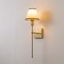 Gold metal wall sconce with beige fabric shade glowing gently on white background for stylish contemporary lighting decor.