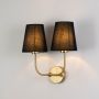 Gold double wall sconce with black fabric shades illuminated on a bright white background for clear visibility.