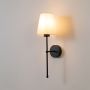 Black wall sconce glowing softly with a white shade on a white background for elegant ambient lighting.