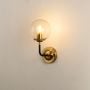 A metal wall light with a clear round glass bulb glowing warmly against a beige wall creating decorative ambient lighting and stylish contemporary décor.