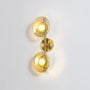 Gold double wall light with amber textured glass globes illuminated on a bright white background for clear visibility.