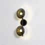 Illuminated black metal wall sconce with glowing smoked glass globe shades emitting warm ambient light on white background.