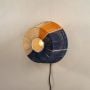Decorative wall lamp with a circular design combining blue and natural fiber panels around a glowing bulb creating a warm artistic focal element in the room.