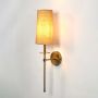 Wall sconce light with golden base and fabric shade turned on glowing softly on white background decor.