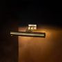 Antique brass picture light with slim tubular design glowing on black background for premium decor styling.