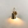 Outdoor wall sconce in brass finish with cone shade turned on glowing softly on white background decor.