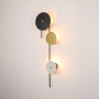 Modern wall light on white background featuring vertical black bar with stacked round discs in black gold and white creating soft ambient glow.