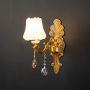 Luxury one light crystal sconce with gold base white shade and crystal drops illuminated on black background.
