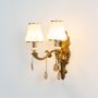 Two light crystal sconce with gold base glowing warmly with white shades and crystal drops on white background.