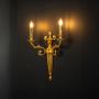Golden wall light with two candle style holders displayed on light black background for modern interiors.