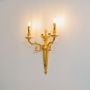 Golden wall light with twin bulb candle style design decorative lighting piece mounted on white background.