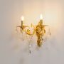 Golden wall light with crystal drops dual candle style decorative wall mounted fixture on white background.