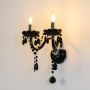 Black wall light with twin candle style and crystal drops elegant decorative fixture on white background.