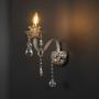 Crystal wall light with glass shade and hanging crystals turned on against black background for home decor.