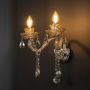 Double arm crystal wall light with glass shades and crystal drops glowing against black background.
