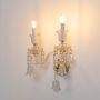 Double arm crystal wall light glowing with gold base glass shades and crystal drops on white background decor.