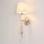 Wall light with chrome base glowing warmly with fabric shade and crystal accents on white background.