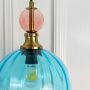Blue glass pendant light closeup showing layered shade detail pink accent globe and brass holder for artistic modern ceiling decor.