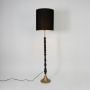 Black floor lamp with tall fabric shade sculpted stem and metal base glowing softly against a clean white background showcasing elegant interior home decor lighting.