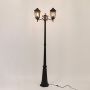 Illuminated black outdoor post lamp with two glowing lantern heads and ornate curved brackets on clean white background.