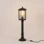 Black outdoor post light with ribbed glass glowing warmly on white background ideal for pathways and garden lighting.