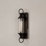 Black metal wall sconce with clear glass tube and ring accents shown on white background for elegant outdoor decor appeal.
