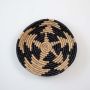 Traditional woven wall basket shown on white background clearly presenting the circular shape detailed weaving pattern and natural black and beige tones.